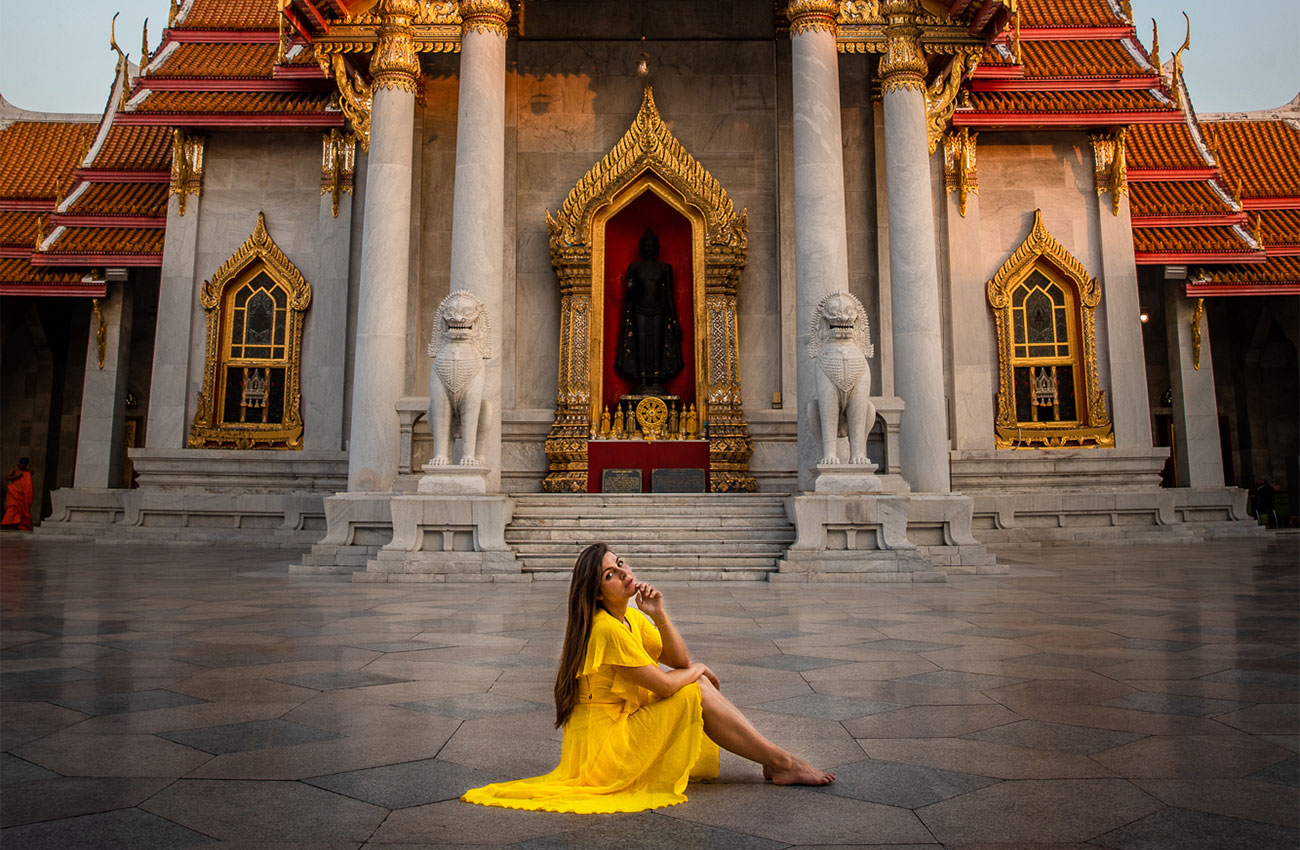 Melissa wearing a bright yellow dress sitting in front of Wat Benchamabopit