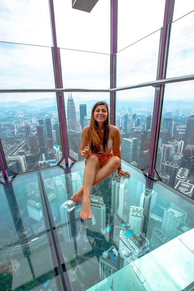 Melissa sits in the glass sky box in the KL tower, smiling.