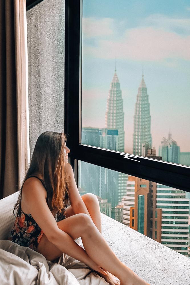 Melissa sits in her hotel bed, looking out the window at the Petronas Towers in KL.